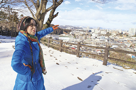 境内から市街地を望む。金野さんが指さす先に、雪をいただいた泉ヶ岳が見えた。